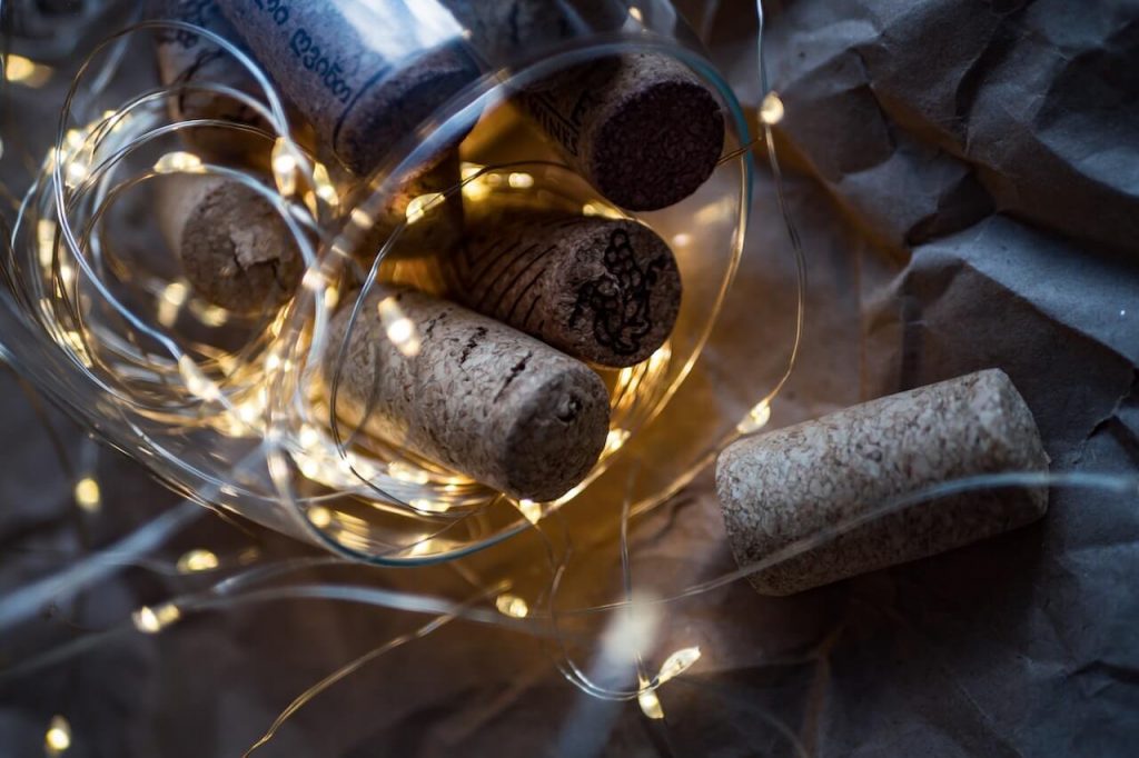 Uma imagem de um copo de vinho com uma colecção de rolhas no interior e rodeado por luzes decorativas.